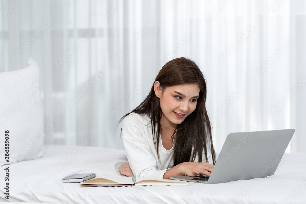 Happy casual beautiful asian woman working on laptop computer while setting  on the bed in the house.