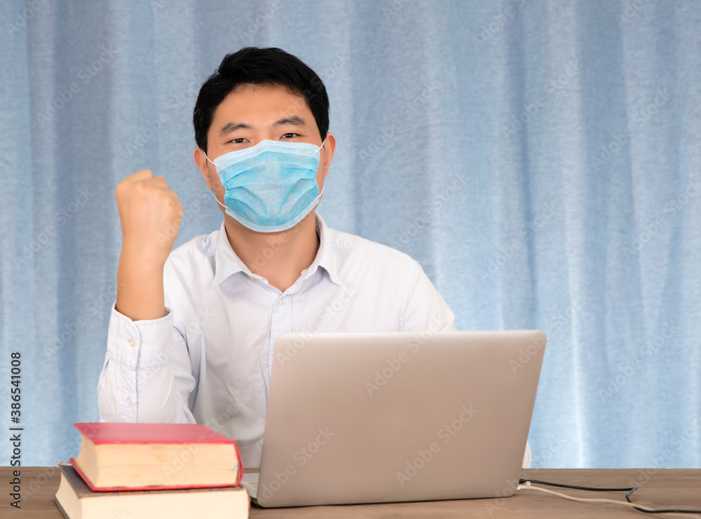 Man wearing a mask at his desk holding his fist Man wearing a mask at his desk holding his fist