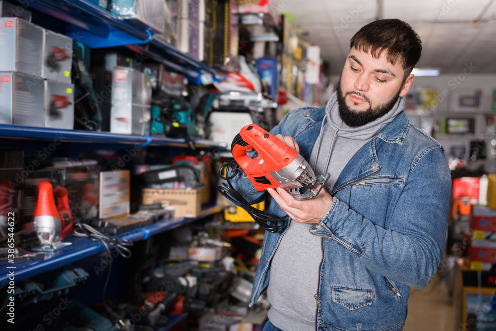 Glad cheerful smiling confident buyer chooses an electric tool in hardware store