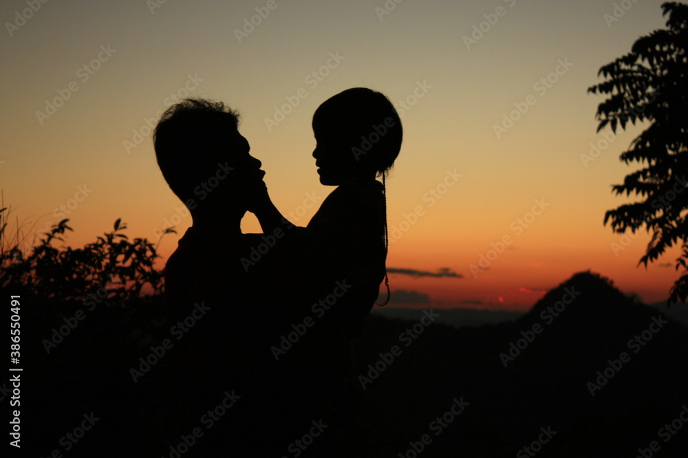 Silhouette of father and son playing on the mountains at the sunset time. Concept of family spending time together on vacation.