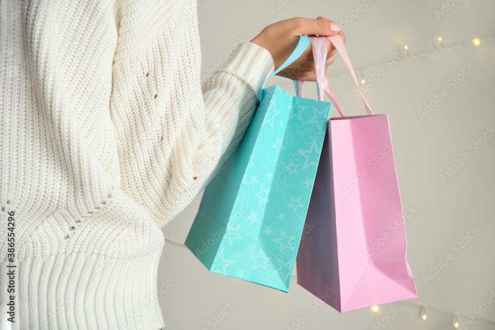 Two gift bags in hand of woman in white sweater on light background with garlands