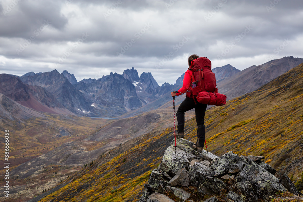 Woman Standing on Rocks looking at Scenic Mountain Peaks and Valley during Fall in Canadian Nature. Taken in Tombstone Territorial Park, Yukon, Canada.