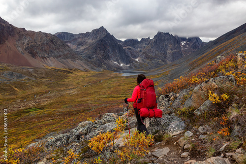 Woman Backpacking on Scenic Rocky Hiking Trail to Lake surrounded by Mountains during Fall in Canadian Nature. Taken in Tombstone Territorial Park, Yukon, Canada.
