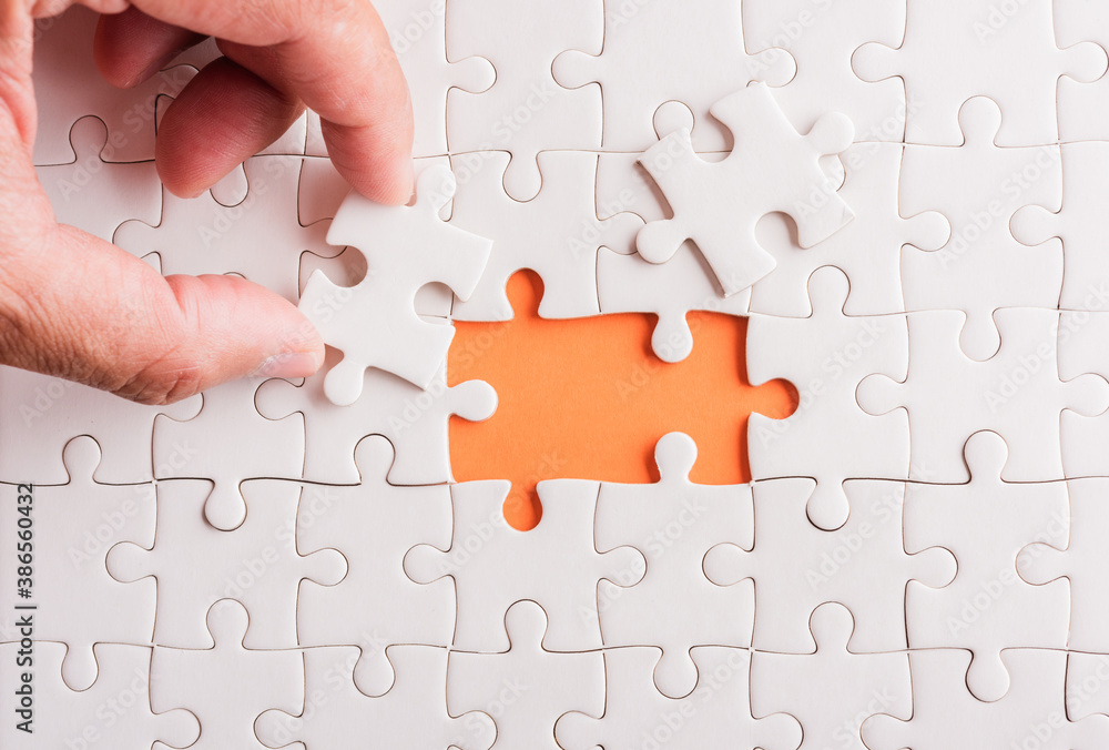 Top view flat lay of hand-holding last piece white paper jigsaw puzzle game last pieces put to place for solve problem complete mission, studio shot on an orange background, quiz calculation concept Top view flat lay of hand-holding last piece white paper jigsaw puzzle game last pieces put to place for solve problem complete mission, studio shot on an orange background, quiz calculation concept