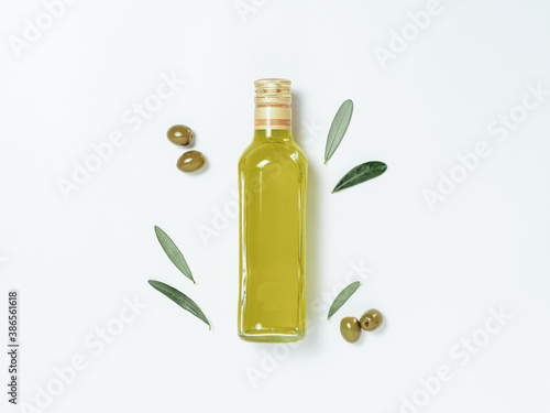Olive oil glass bottle mock up. Top view of clear glass bottle with olive oil on white background with green olives and fresh green olive tree leaves. Copy space. photo