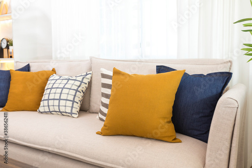 Obraz na plátně Blue and yellow pillows on a white sofa with glass vase and plant pot on table, living room interior