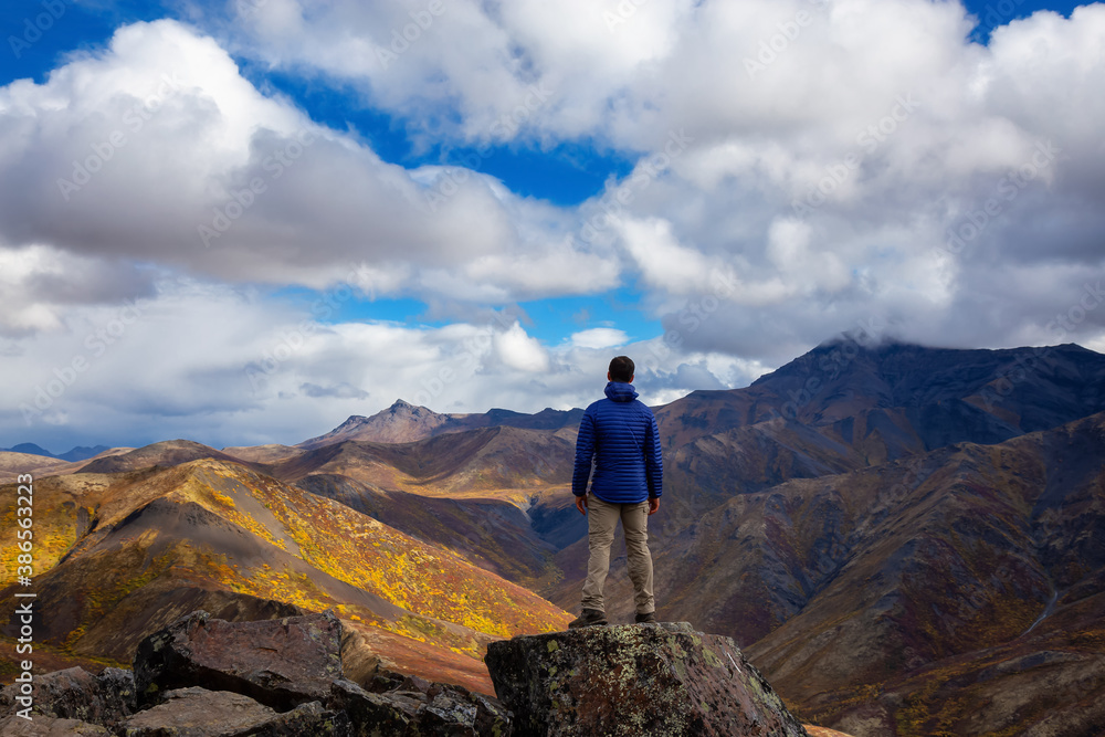 Man Standing and Looking at Viewpoint of Mountain Range on a Cloudy Fall Day in Canadian Nature. Taken in Tombstone Territorial Park, Yukon, Canada. Man Standing and Looking at Viewpoint of Mountain Range on a Cloudy Fall Day in Canadian Nature. Taken in Tombstone Territorial Park, Yukon, Canada.
