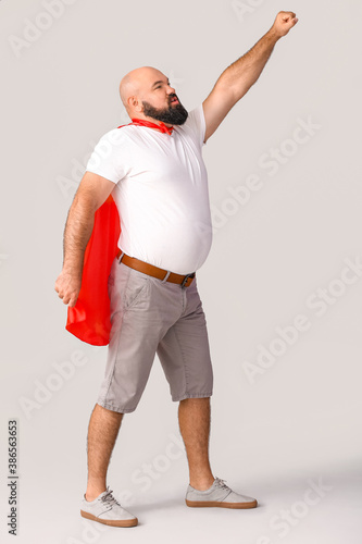 Overweight man in cape on grey background. Weight loss concept