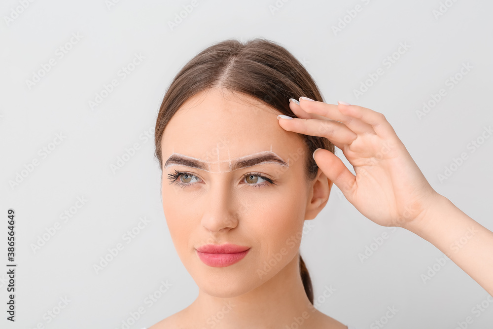 Young woman with marking for eyebrow correction against light background