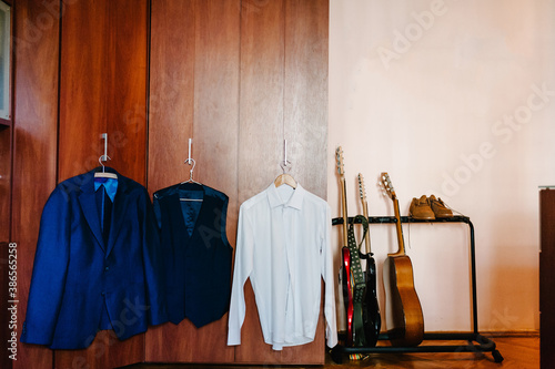 Jacket, shirt, groom's shoes on background of musician's room. Guitars. Stylish menswear. White shirt and blue jacket on the hanger. classic style.