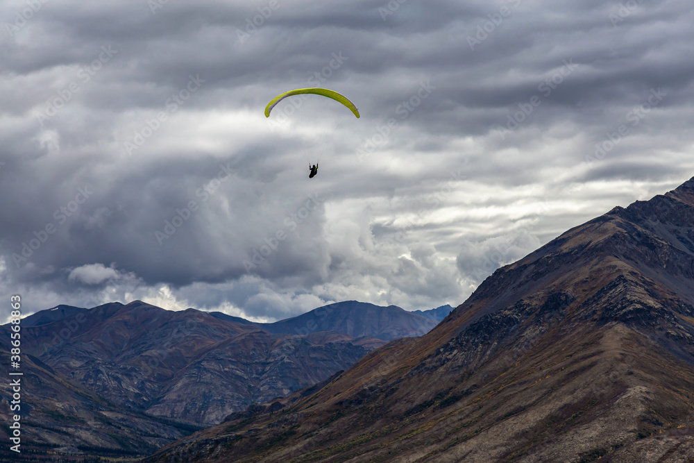 Paraglider flying over Scenic Mountain Range in Canadian Nature. Taken in Tombstone Territorial Park, Yukon, Canada.