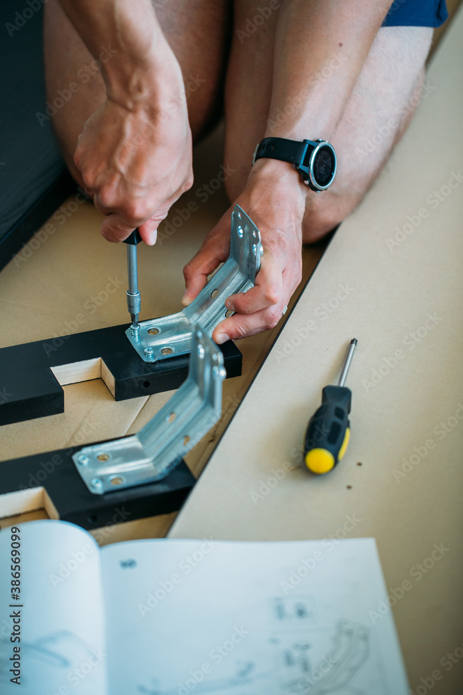 Shallow focus images of man assembling furniture at home using a  screwdriver.