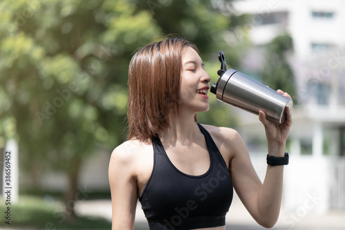Sports woman drinks protein shake from stainless steel blender bottle shaker on natural green background.