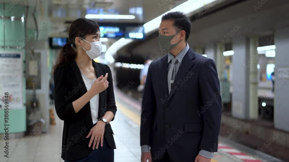 Japanese business woman and man wearing face mask talk while waiting in subway station. Medium shot. Japanese business woman and man wearing face mask talk while waiting in subway station. Medium shot.