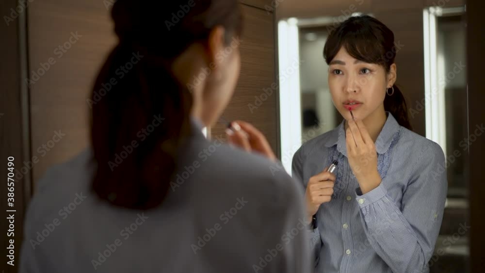 Japanese business woman using lipstick looking in the mirror. Asian female puts on makeup before work. Japanese business woman using lipstick looking in the mirror. Asian female puts on makeup before work.