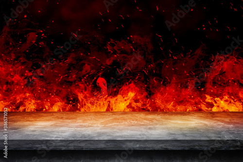 Side view of Empty concrete table top with orange fire or flame and sparkles in dark room. © Angkana