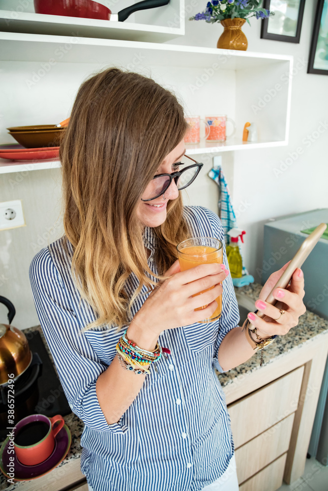 Modern young woman using cellphone in the kitchen. Modern young woman using cellphone in the kitchen.