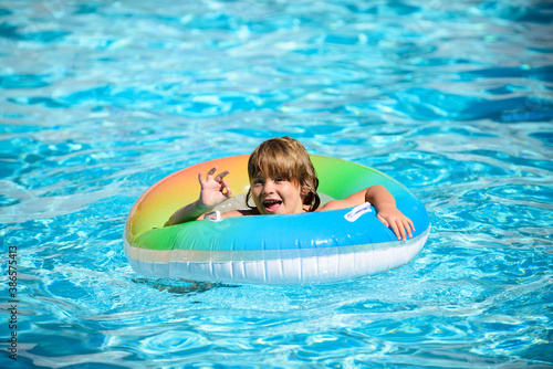 Happy kid playing with colorful swim ring in swimming pool on summer day. Child water toys. Children play in tropical resort. Family beach vacation.