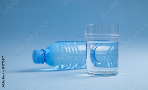 Plastic water bottle and glass of water on blue background.