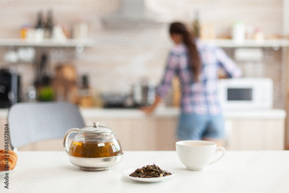 Woman preparing breakfast in kitchen and aromatic herbs for hot tea. Shot with background blur of lady having great morning with tasty natural healthy herbal tea sitting in the kitchen.