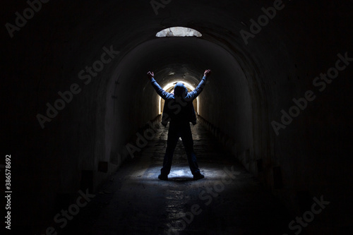 A man in a dark underground tunnel is looking for a way out and raises his hands to the sky asking for help.