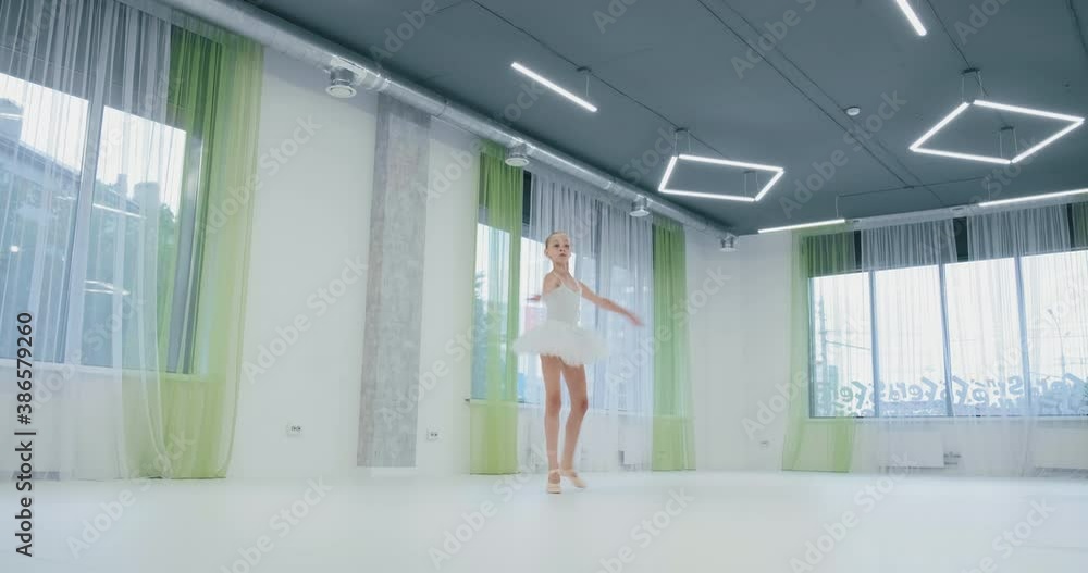 beautiful little ballerina in white suit with tutu performs classical dance in studio with large windows beautiful little ballerina in white suit with tutu performs classical dance in studio with large windows