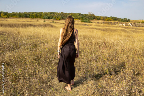 Pretty young dark haired woman in black dress stand in field. Beautiful girl outdoor in the field enjoy with freedom
