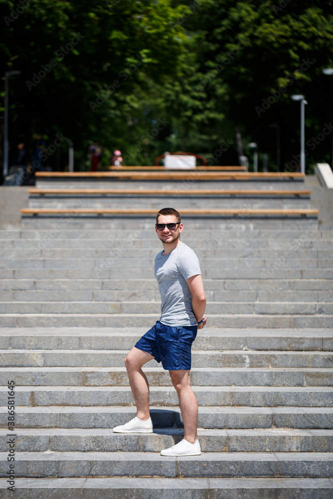 A handsome man in a T-shirt and shorts stands on the steps. Guy in sunglasses A handsome man in a T-shirt and shorts stands on the steps. Guy in sunglasses