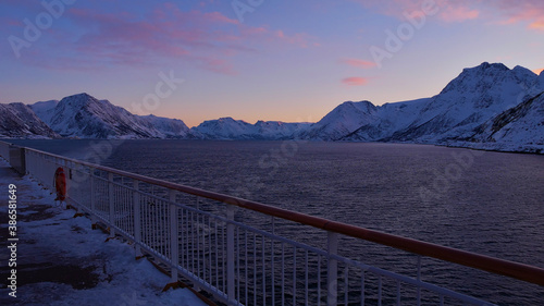 Winterly view of the arctic ocean and snow-covered mountains from the upper deck of a cruise ship near Øksfjord, Norway, Scandinavia in evening light with beautiful colored clouds.