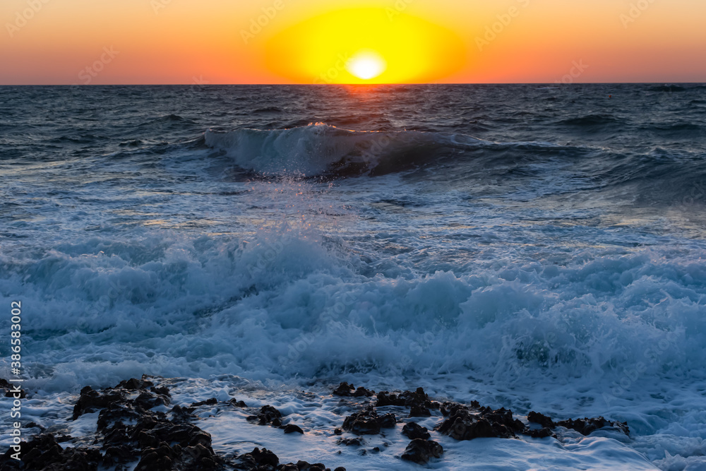 Sunset and storm at sea. Big waves against the setting sun. Summer storm on the Black sea. Beautiful sea spray with foam breaks on the rocky shore. Beautiful sea background. Orange setting sun.
