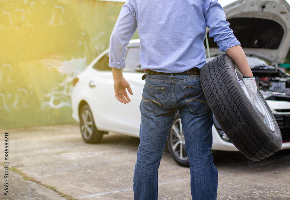 Obraz premium An Asian man is holding his spare tire ready to replace it after his car has a roadside puncture.