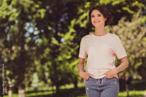 Photo of sweet adorable young girl lady beaming smile hands pockets look side meet friends walk park garden spend free time day off shiny spring summer day wear beige t-shirt jeans outside