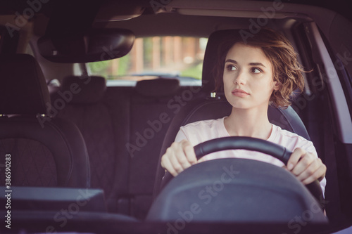 Photo of cute pretty lady serious calm face hands steering wheel look rearview mirror parking try not scratch other cars careful concentrated smart moves wear white shirt indoors