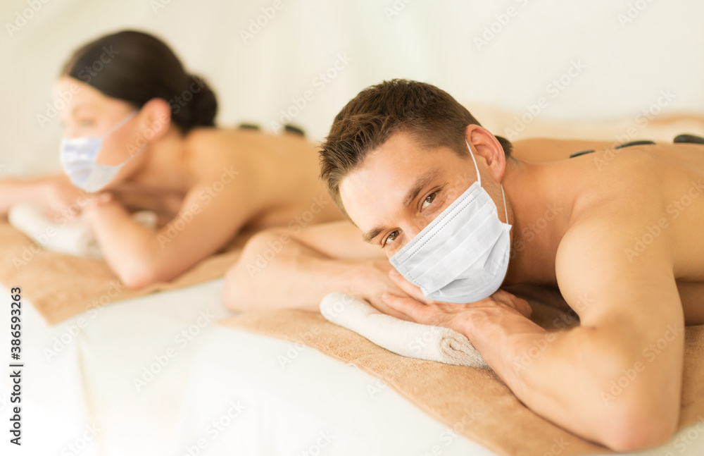 wellness, bodycare and health concept - couple wearing face protective medical masks for protection from virus disease at spa