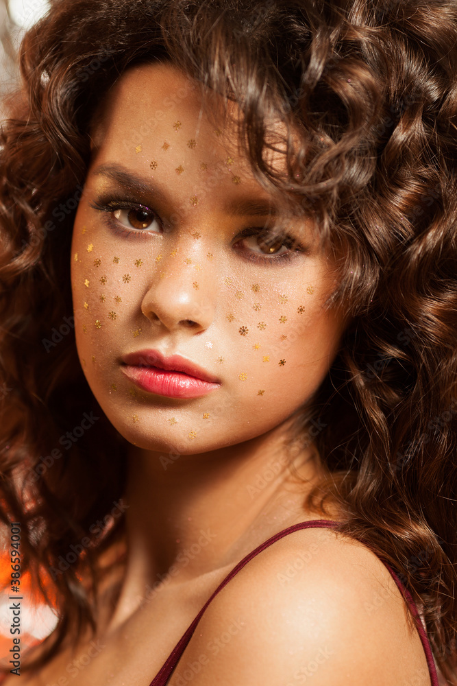 Fototapeta premium Creative winter makeup with golden snowflakes on her face and wavy hairstyle