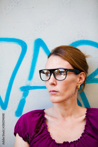 Urban portrait of a dark haired woman with glasses looking away. Graffiti background.