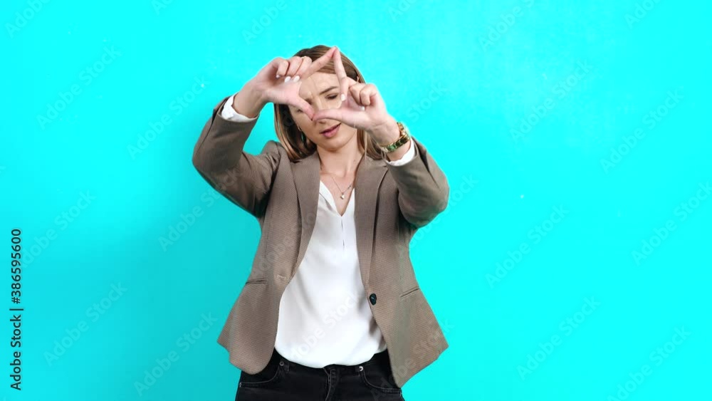 Concentrated inspired businesswoman in suit looking for a suitable angle for shooting, looking through the fingers in the form of frame, creativity. Studio image indoors, isolated on blue background Concentrated inspired businesswoman in suit looking for a suitable angle for shooting, looking through the fingers in the form of frame, creativity. Studio image indoors, isolated on blue background
