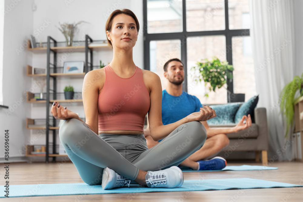 fitness, people and healthy lifestyle concept - man and woman meditating in yoga lotus pose at home fitness, people and healthy lifestyle concept - man and woman meditating in yoga lotus pose at home