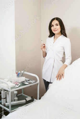 Cosmetologist. Doctor holding a syringe for beauty injection. Portrait of young female friendly beautician on the background of the office in medical cosmetology clinic