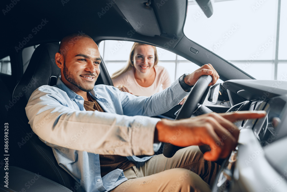 Joyful young couple looking around inside a new car they are going to buy in a car shop Joyful young couple looking around inside a new car they are going to buy in a car shop