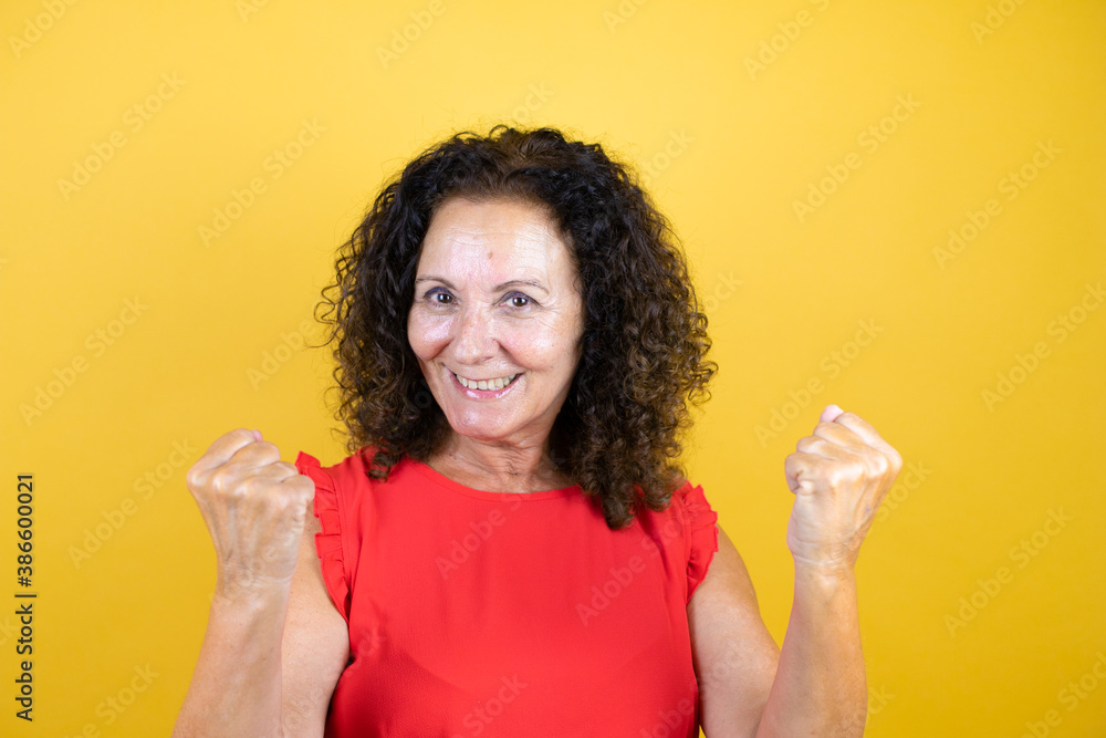 Middle age woman wearing casual shirt standing over isolated yellow background very happy and excited making winner gesture with raised arms, smiling and screaming for success. Middle age woman wearing casual shirt standing over isolated yellow background very happy and excited making winner gesture with raised arms, smiling and screaming for success.