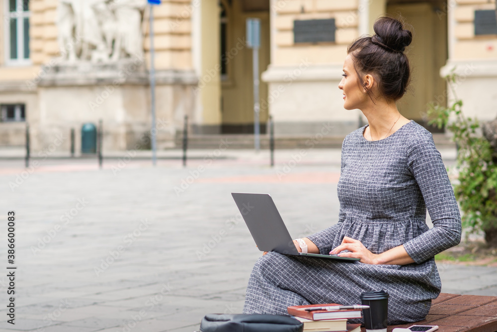 Student young woman uses laptop on the bench on the city street near university Student young woman uses laptop on the bench on the city street near university