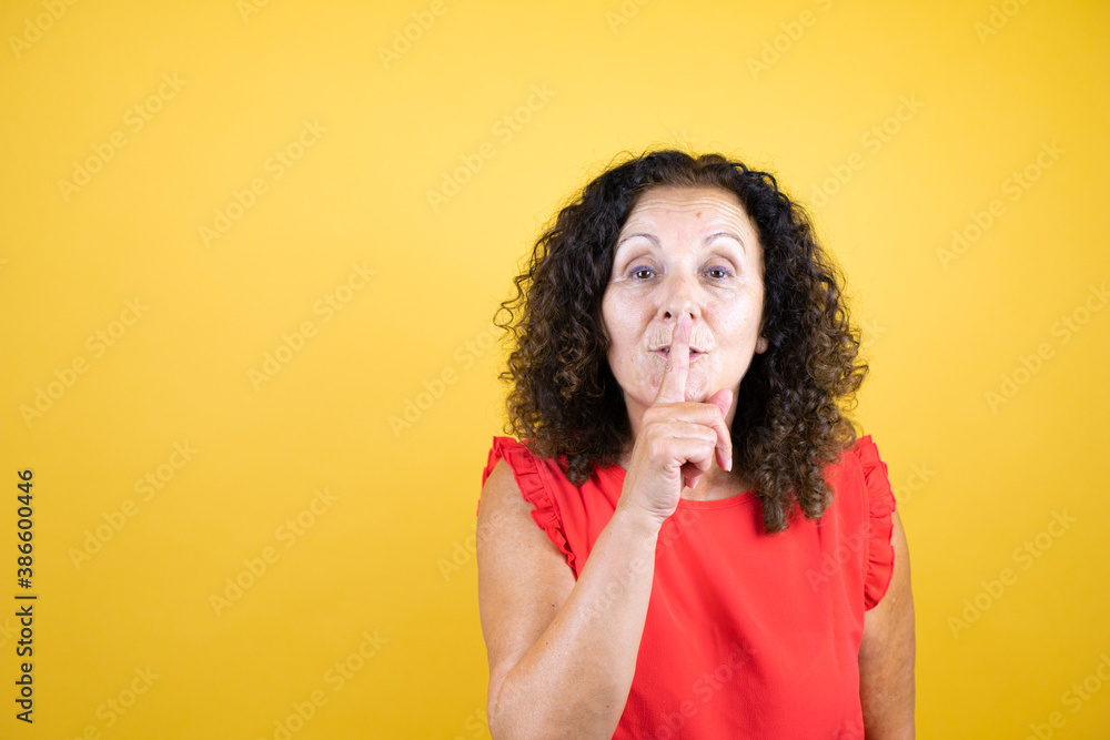 Middle age woman wearing casual shirt standing over isolated yellow background asking to be quiet with finger on lips. Silence and secret concept. Middle age woman wearing casual shirt standing over isolated yellow background asking to be quiet with finger on lips. Silence and secret concept.