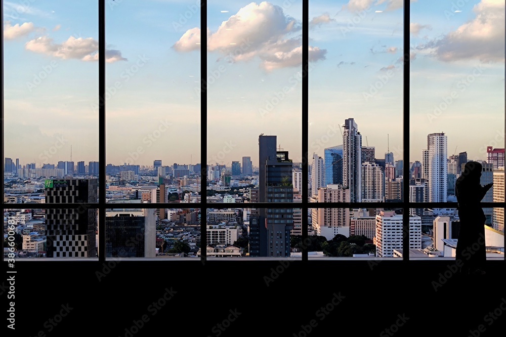 silhouette outline of women tourist taking pictures of city skyline from an observatory. sunset at modern urban business district. steel frame rose windows architectural element design.