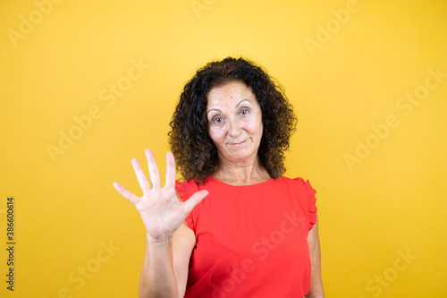 Middle age woman wearing casual shirt standing over isolated yellow background showing and pointing up with fingers number five while smiling confident and happy