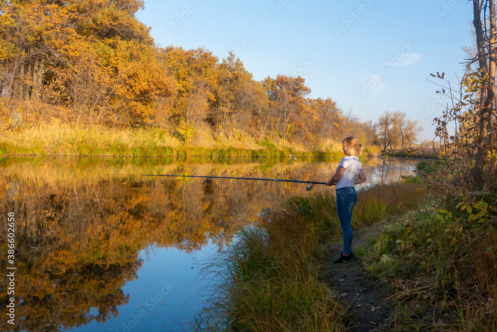 Fishing in autumn on the river. Young woman holds fishing rod above surface of water