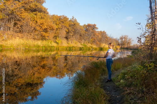Fishing in autumn on the river. Young woman holds fishing rod above surface of water
