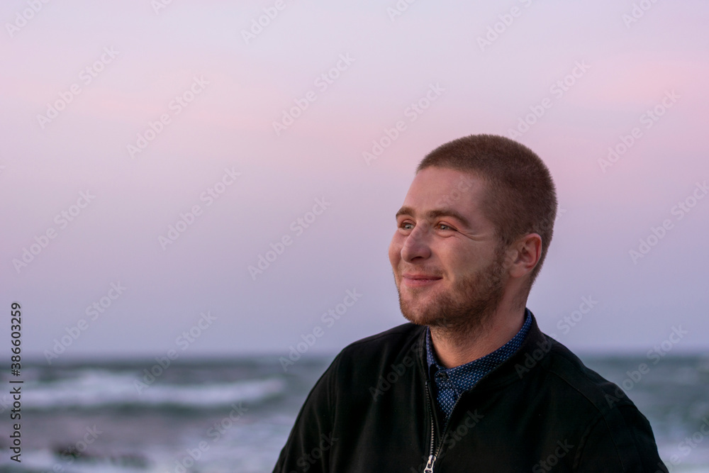 Smiling young Caucasian man with beard on background of the sea and waves with white foam. Selective focus, close-up Smiling young Caucasian man with beard on background of the sea and waves with white foam. Selective focus, close-up