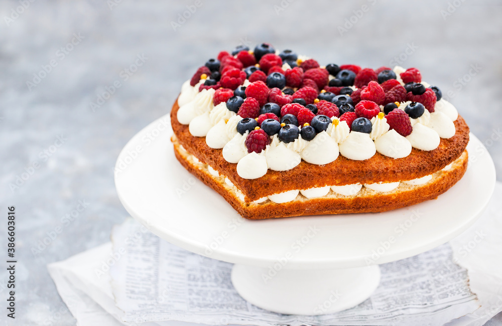 Delicious homemade heart shaped vanilla cake decorated with cream and fresh berries