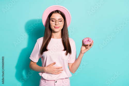 Portrait of her she nice attractive dreamy cheery brown-haired girl eating pink fresh doughnut touching caressing belly stomach isolated bright vivid shine vibrant green turquoise color background